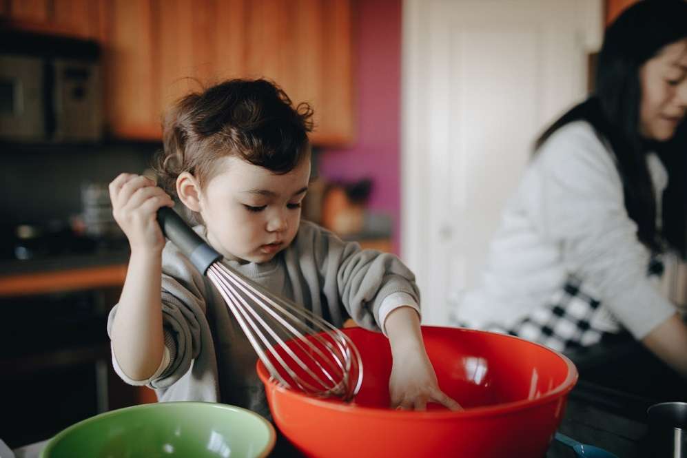little boy using a whisk in the kitchen.