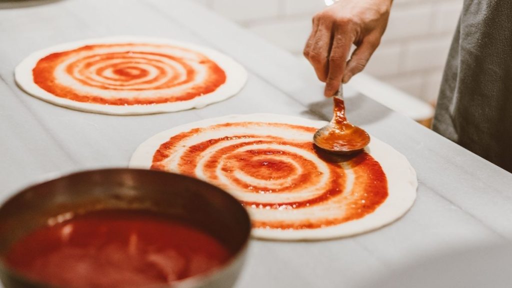 A person putting sauce on a pizza