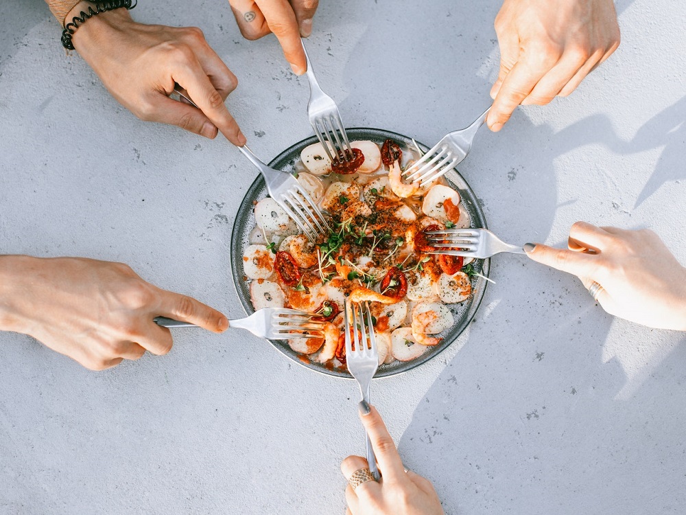 5 hands around a seafood dinner plate